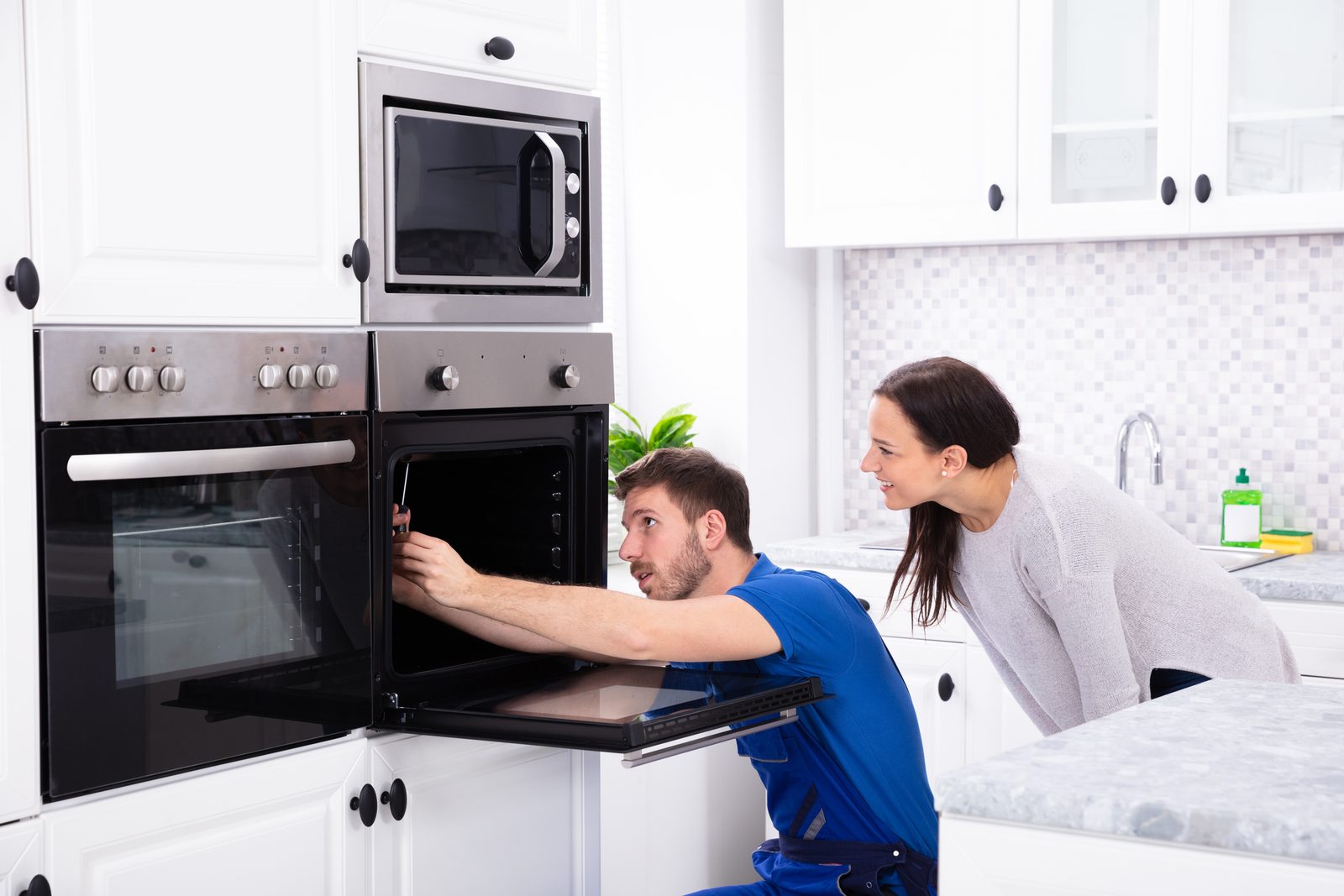 Technicien réparant un four encastrable dans une cuisine, en présence de la cliente